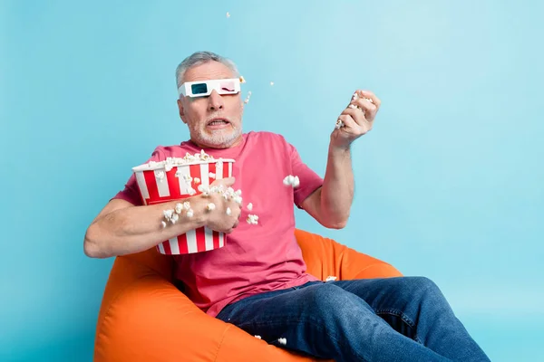 Portrait of attractive funky worried man sitting in chair eating corn free time isolated over bright blue color background — Stock Photo, Image