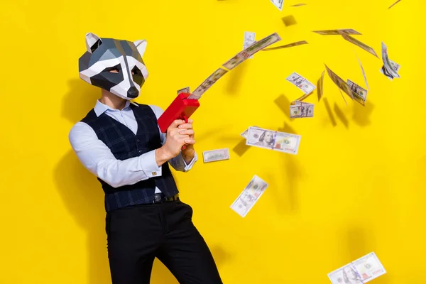 Fénykép őrült srác mosómedve maszk ünneplés halloween lő pisztoly profit pénz elszigetelt sárga élénk szín háttér — Stock Fotó