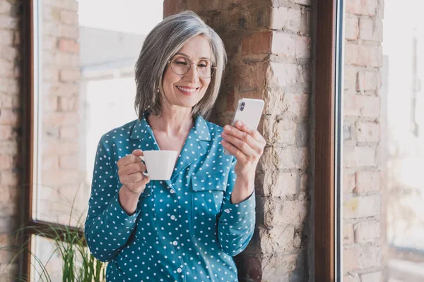 Foto di donna anziana dai capelli grigi tenere telefono tazza usura formalwear all'interno di postazione di lavoro ufficio — Foto Stock