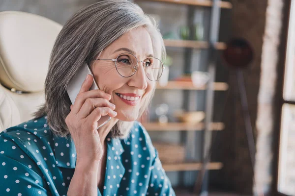 Фото позитивной веселой пожилой женщины смотреть в сторону держать телефонный разговор разговор улыбка в помещении офиса — стоковое фото