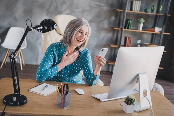 Fotografie veselý radostný šťastný šedovlasá stará dáma úsměv vzhled telefonu uvnitř kanceláře pracoviště — Stock fotografie
