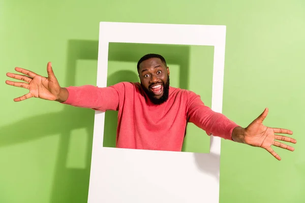 Portrait of overjoyed handsome man raise arms through photo card frame isolated on green color background — Stockfoto