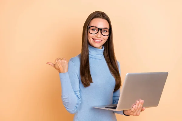 Foto di smart bruna giovane signora tenere indice del computer portatile promo usura occhiali blu dolcevita isolato su sfondo di colore beige — Foto Stock