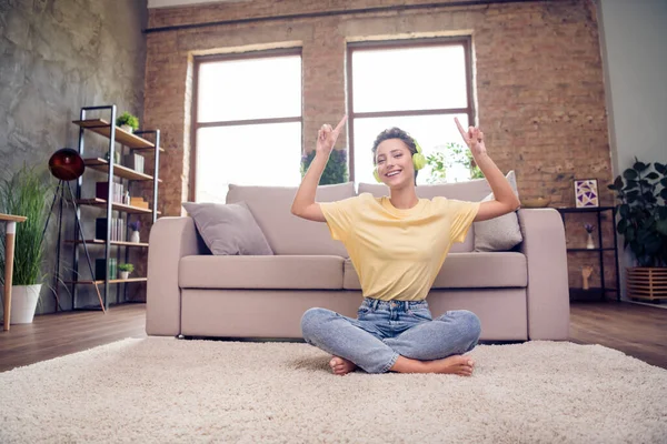 Foto van zorgeloze dromerige dame zit vloer genieten luisteren muziek dans dragen oortjes geel t-shirt in modern huis binnen — Stockfoto