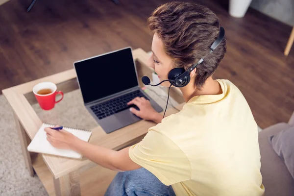 Foto van gerichte remote receptioniste dame zitten laptop schrijven notitieblok dragen headset geel t-shirt in modern huis binnen — Stockfoto