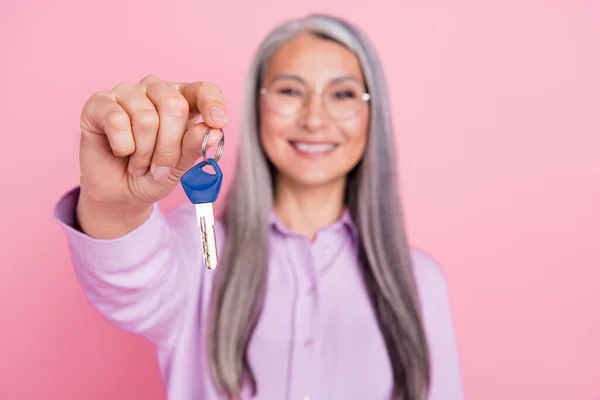 Retrato de mulher de cabelos grisalhos alegre atraente dando quarto chave da casa do hotel isolado sobre fundo cor pastel rosa — Fotografia de Stock