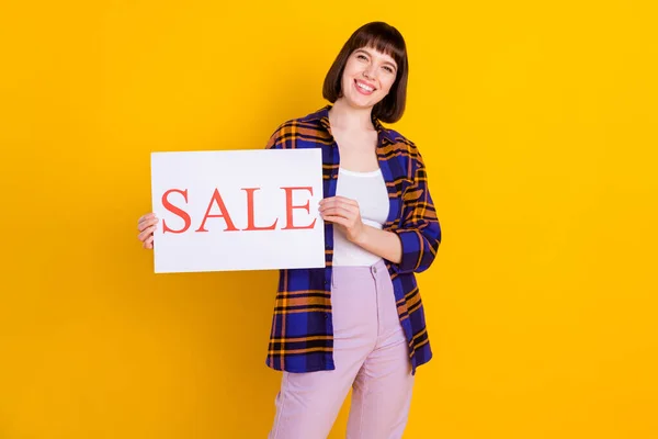 Portret van aantrekkelijk vrolijk meisje dragen geruite shirt houden in handen verkoop woord bordje geïsoleerd over helder gele kleur achtergrond — Stockfoto