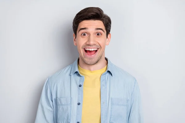 Foto av sjarmerende, imponert ung mann med jeans skjorten smilende åpen munn, isolert grå farge bakgrunn – stockfoto