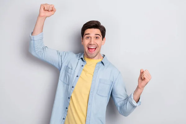 Foto van geluk onder de indruk jonge man dragen jeans shirt rijzende vuisten open mond geïsoleerde grijze kleur achtergrond — Stockfoto