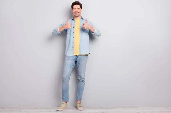 Zdjęcie pewny siebie młody facet nosić dżinsy koszula pokazując kciuki w górę puste miejsce odizolowany beton szary ściana tło — Zdjęcie stockowe