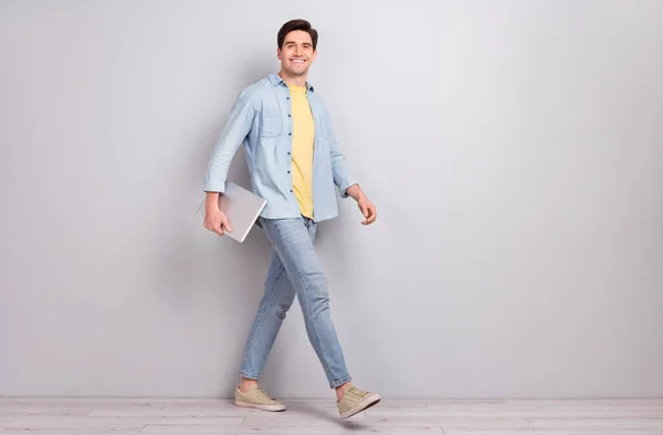 Фото позитивного веселого парня носить джинсовую рубашку держа гаджет пустое место изолированный бетонный фон серой стены — стоковое фото