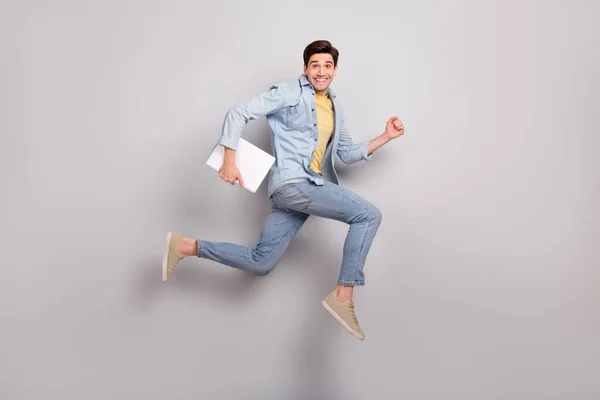 Foto de cara engraçado atraente vestido camisa jeans segurando dispositivo saltando alto isolado fundo de cor cinza — Fotografia de Stock
