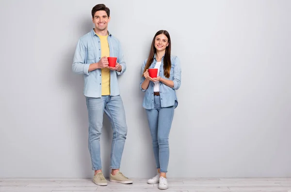 Foto di dolce affascinante sorella fratello vestito camicie denim bere tes isolato cemento grigio muro fondo — Foto Stock