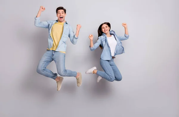 Foto van gelukkige broer zus dragen jeans shirts rijzende vuisten springen hign geïsoleerd beton grijze muur achtergrond — Stockfoto