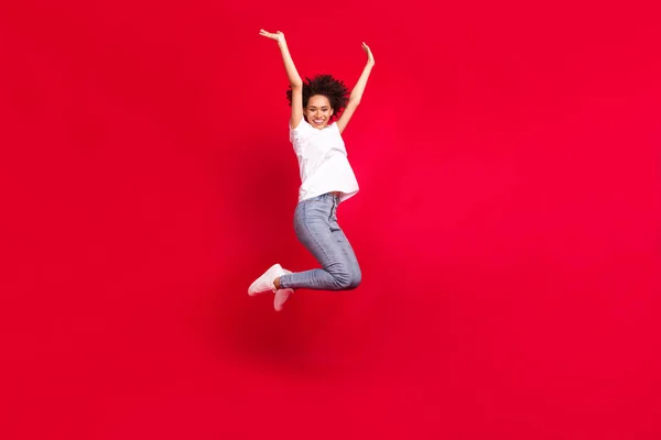 全长体形照片，微笑着卷曲的女人跳跃着，像获胜者一样摆姿势，孤立的鲜红的背景 — 图库照片