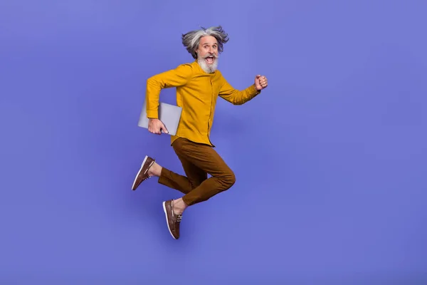 Longitud completa vista del tamaño del cuerpo del hombre barbudo de pelo gris de moda saltar sosteniendo portátil aislado en el brillo violeta púrpura color de fondo —  Fotos de Stock