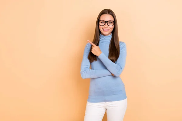 Photo of optimistic brunette millennial lady index empty space wear eyewear blue pullover isolated on beige color background — Foto Stock