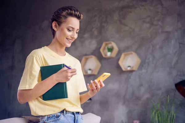 Fénykép bájos pozitív hölgy hold copybook telefon chat kopás sárga póló a modern házban beltéri — Stock Fotó