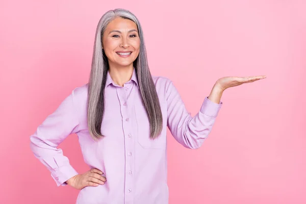 Ritratto di attraente allegra donna dai capelli grigi che tiene copia spazio vuoto offerta annuncio isolato su sfondo di colore rosa pastello — Foto Stock