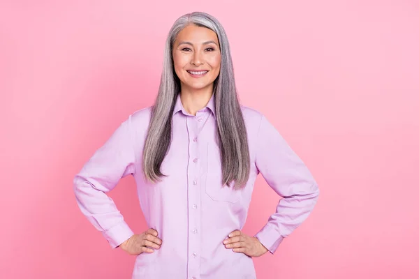 Portret van aantrekkelijke vrolijke succesvolle grijs-harige vrouw handen op heupen geïsoleerd over roze pastel kleur achtergrond — Stockfoto