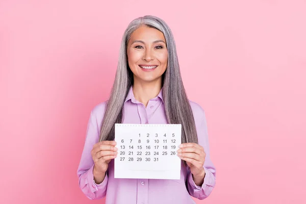 Ritratto di attraente donna dai capelli grigi che tiene in mano il calendario isolato su sfondo di colore rosa pastello — Foto Stock