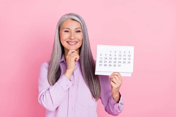 Ritratto di attraente felice allegra donna dai capelli grigi in possesso di calendario nuovo anno isolato su sfondo rosa pastello — Foto Stock