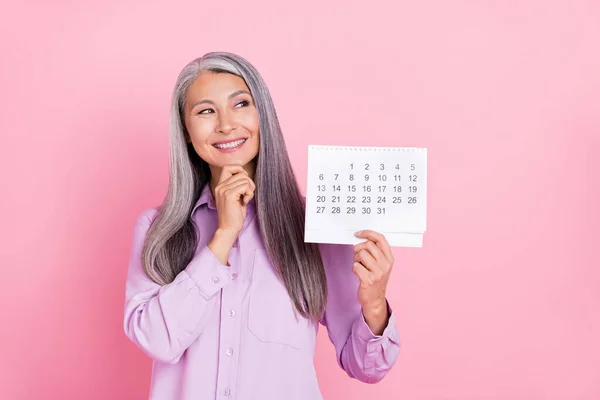 Ritratto di attraente mentalità allegra donna dai capelli grigi che tiene il calendario pensando isolato su sfondo di colore rosa pastello — Foto Stock
