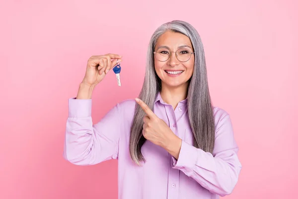 Retrato de atraente na moda alegre mulher de cabelos grisalhos segurando demonstrando chave da casa isolada sobre fundo cor pastel rosa — Fotografia de Stock