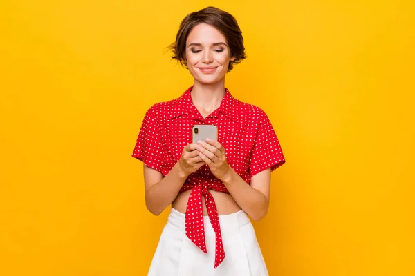 Foto de una joven bastante feliz y sonriente bloguera de chicas positivas en top rojo usando un teléfono inteligente aislado sobre un fondo de color amarillo —  Fotos de Stock
