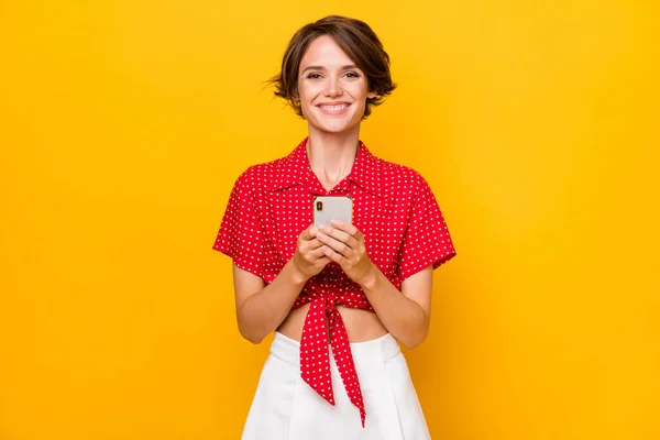 Foto de mujer morena agradable optimista sostener teléfono usar camisa falda aislada sobre fondo de color amarillo —  Fotos de Stock