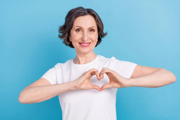 Porträt von attraktiven fröhlichen grauhaarigen Frau zeigt Herzzeichen Pflege isoliert über helle blaue Farbe Hintergrund — Stockfoto