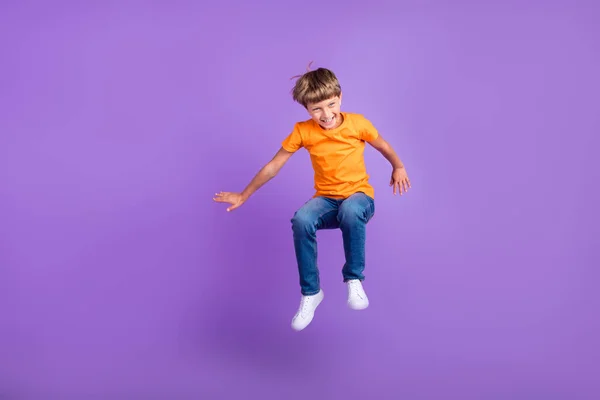 Повна довжина тіла фото хлопчика, який стрибає сміючись, насолоджуючись ізольованим пастельно-фіолетовим кольоровим фоном — стокове фото