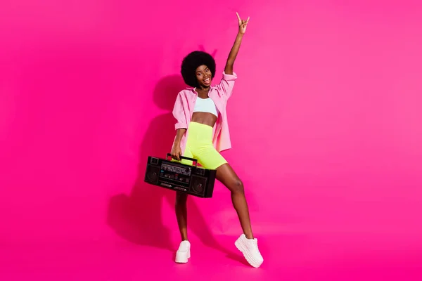 ファンキーでかわいい黒い肌の女性の写真は、ブームボックスを保持ダンスカジュアルシャツを身に着けている指笑顔孤立ピンク色の背景を指す — ストック写真