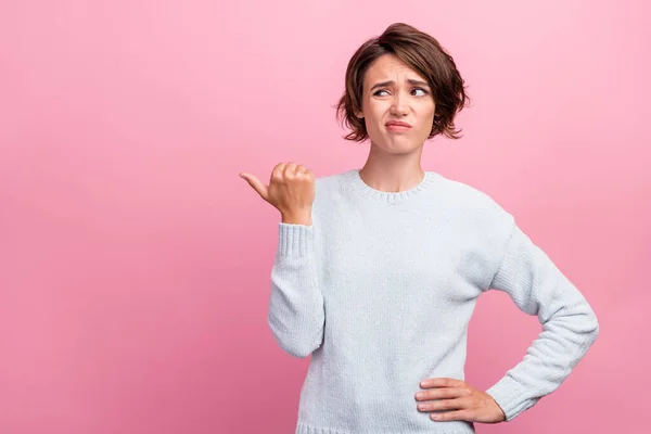 Photo of unhappy upset doubtful young woman point finger empty space thumb dislike isolated on pink color background — 图库照片