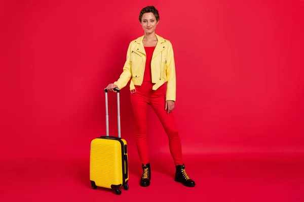 Foto de encantadora linda dama joven usar chaqueta amarilla sonriendo equipaje de bodega listo para el viaje aislado de color rojo de fondo —  Fotos de Stock