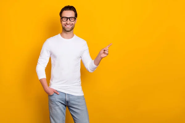 Fotografie optimistický brunet tisíciletý chlap index prázdný prostor nosit brýle bílé oblečení izolované na pulzující žluté barvy pozadí — Stock fotografie