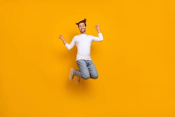 Full length photo of cool brunet młody facet skakać ręce pięści nosić koszulę dżinsy obuwie izolowane na żółtym tle — Zdjęcie stockowe