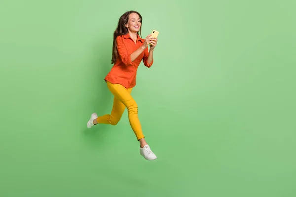 Photo of sweet charming young woman wear red shirt smiling jumping high communicating modern gadget isolated green color background — Stockfoto