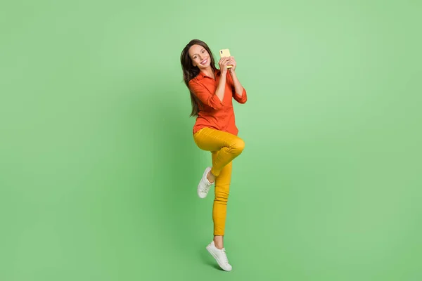 Foto av rolig söt ung kvinna bära röd skjorta ler hoppa högt chatta modern gadget isolerad grön färg bakgrund — Stockfoto
