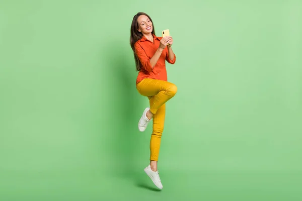 Foto di bella signora matura funky vestita camicia rossa digitando dispositivo moderno salto alto sorridente isolato sfondo di colore verde — Foto Stock