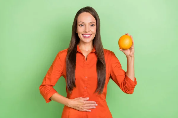 Foto de encantadora señora bastante madura vestida camisa roja que sostiene jugoso brazo naranja estómago sonriendo aislado color verde fondo — Foto de Stock