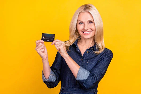Foto von charmanten hübschen Rentnerin tragen Jeans Kleidung mit Kreditkarte isoliert gelben Hintergrund — Stockfoto