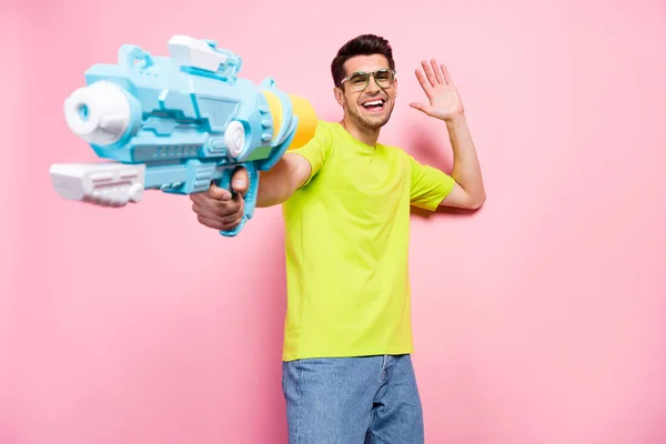 Portrait of attractive cheerful guy shooting water weapon having fun fooling party isolated over pink pastel color background — Stockfoto