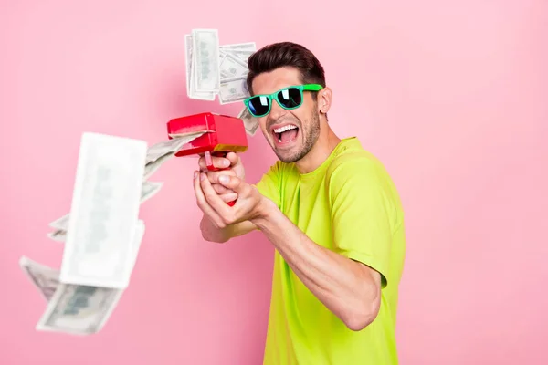 Φωτογραφία πορτρέτο τρελός άνδρας φορώντας φωτεινό t-shirt γυρίσματα με τραπεζογραμμάτια από όπλο απομονωμένο παστέλ ροζ χρώμα φόντο — Φωτογραφία Αρχείου