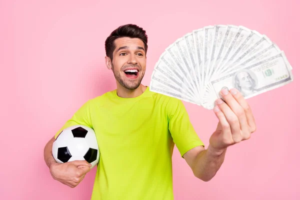 Foto portret voetbal fan het dragen van heldere t-shirt houden voetbal bankbiljetten stapel geïsoleerde pastel roze kleur achtergrond — Stockfoto