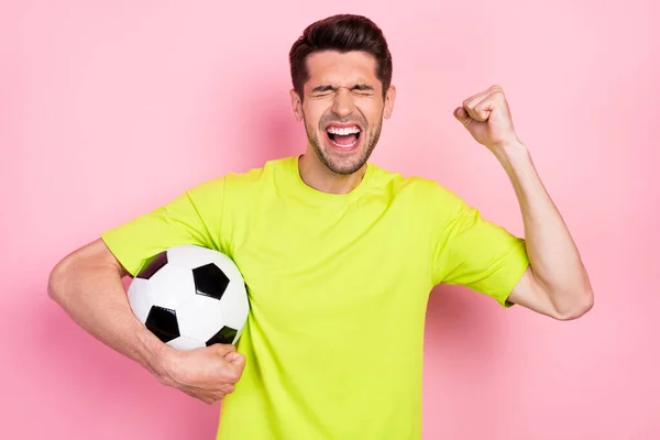 Фотопортрет кричащий человек в яркой футболке держит футбольный мяч жестом, как победитель изолированный пастельно-розовый цвет фона — стоковое фото
