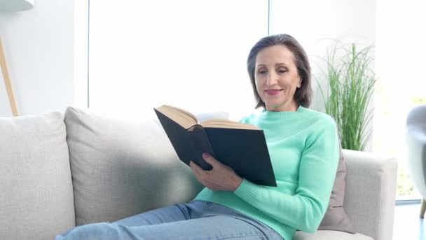 Señora de mediana edad leer abrazo abrazo libro favorito sentarse diván en la sala de estar — Vídeo de stock