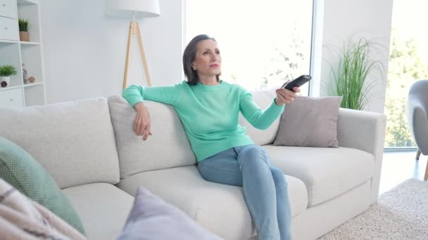 편안 한 중년 부인 이 아파트에 앉아 디 반 선택 채널 장치를 보고 있다 — 비디오