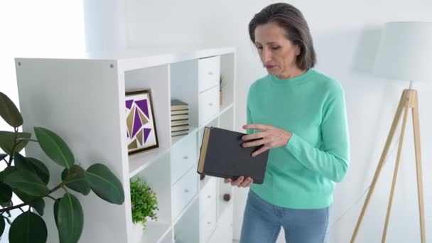Mulher de meia idade segurar livro interessante sentar divã no interior do apartamento — Vídeo de Stock