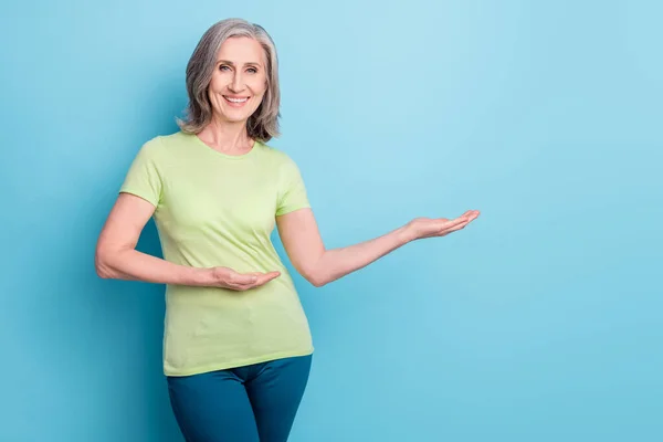 Foto de mulher velha alegre atraente segurar as mãos espaço vazio decidir produto isolado no fundo de cor azul — Fotografia de Stock